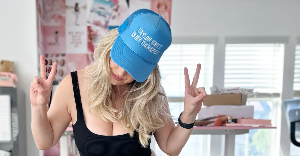 Sarah Komers wearing a blue “Taylor Swift Is My Therapist” cap and holding up peace signs.