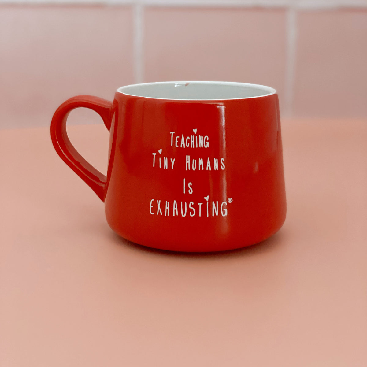 Red ceramic mug with white “Teaching Tiny Humans Is Exhausting” lettering.