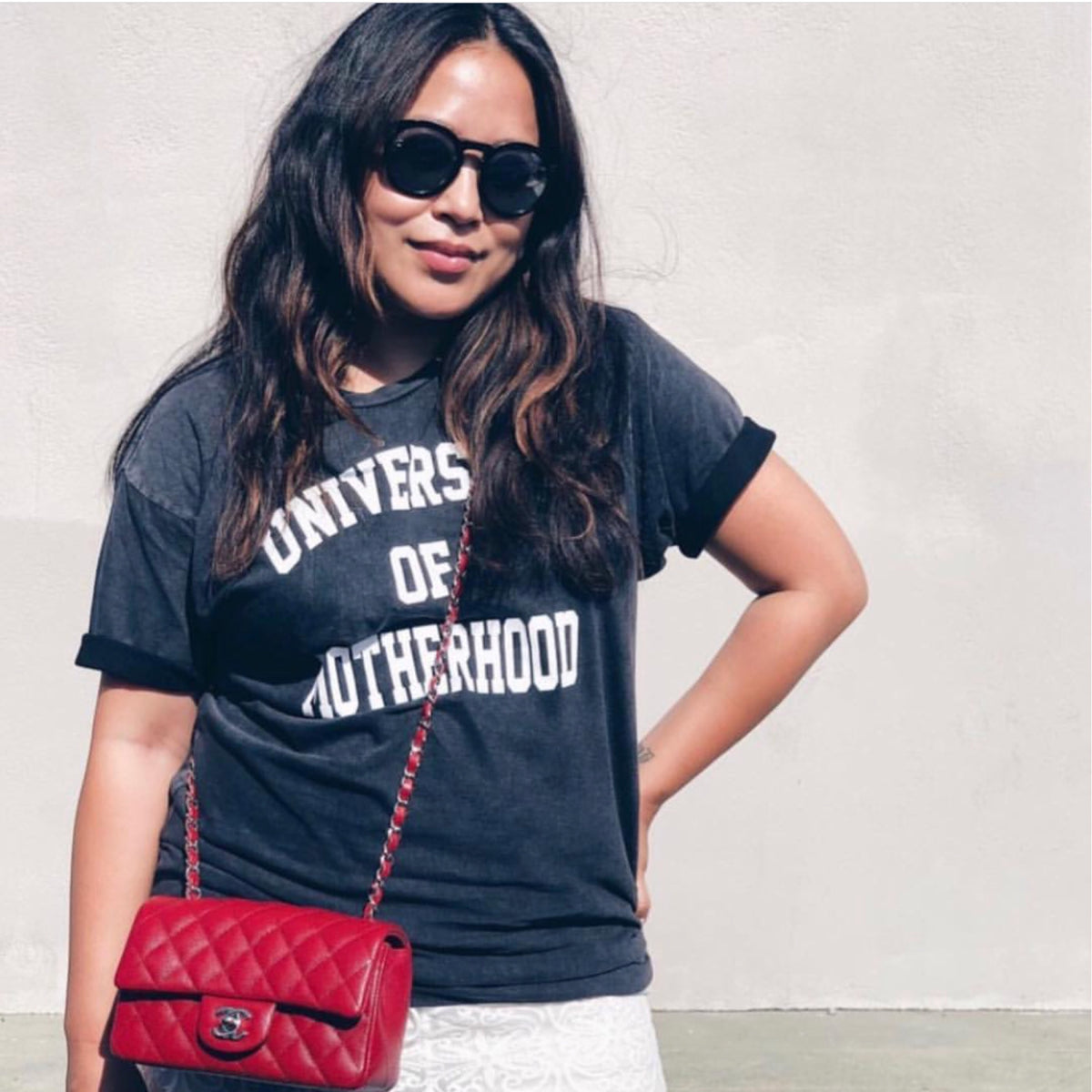 Woman wearing a black “University of Motherhood” T-shirt and a red crossbody bag.