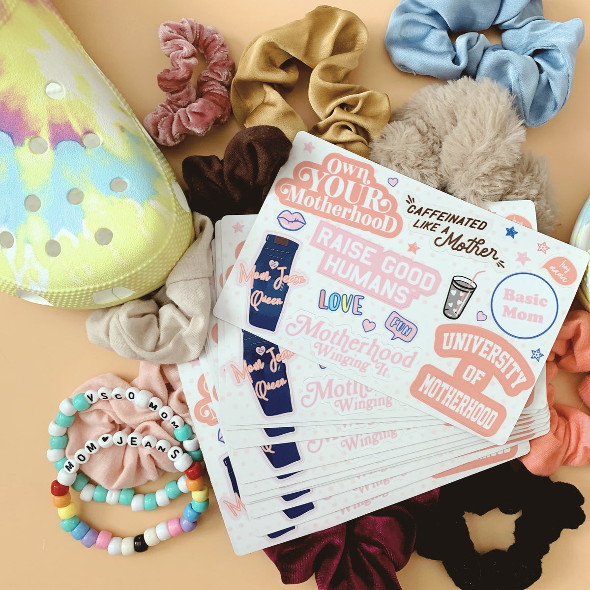Mom Culture sticker sheets surrounded by scrunchies and colorful bracelets.