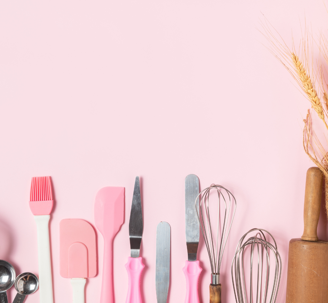 Pink spatulas, whisks and other kitchen utensils against a pink background.