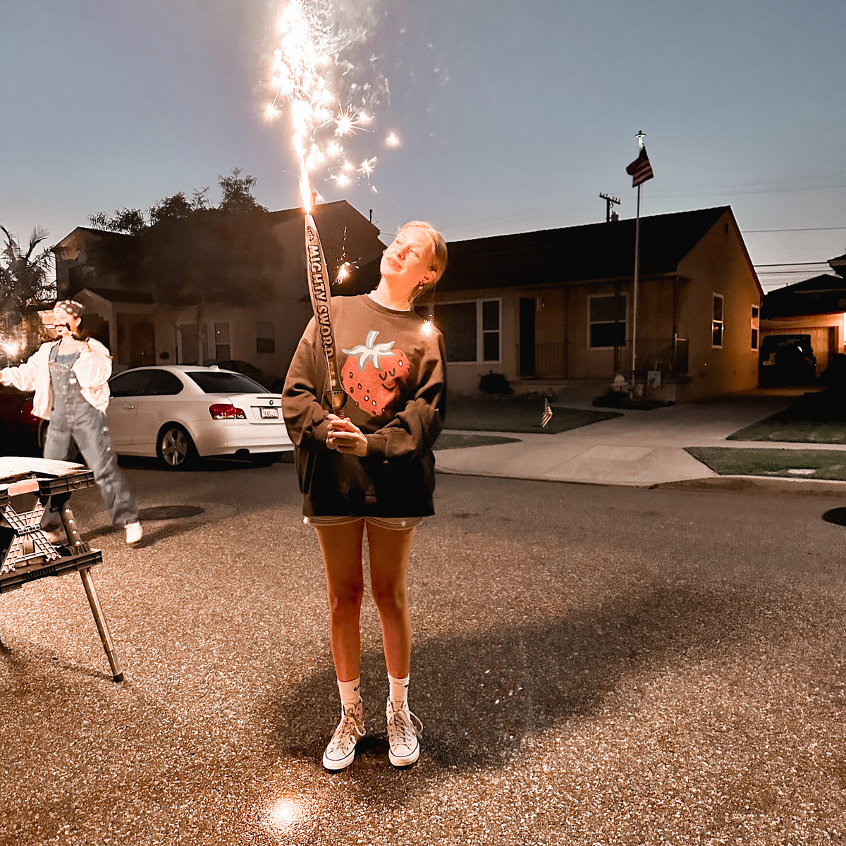 Person holding a lit sparkler in a driveway on the Fourth of July.
