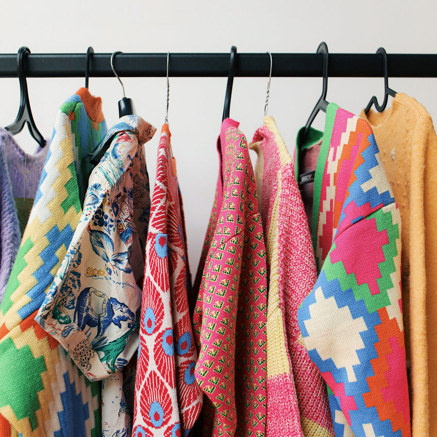 Colorful patterned clothing hanging on a black rail.