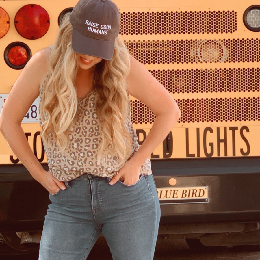 Woman wearing a “Raise Good Humans” cap and jeans in front of a wall of vehicle lights.