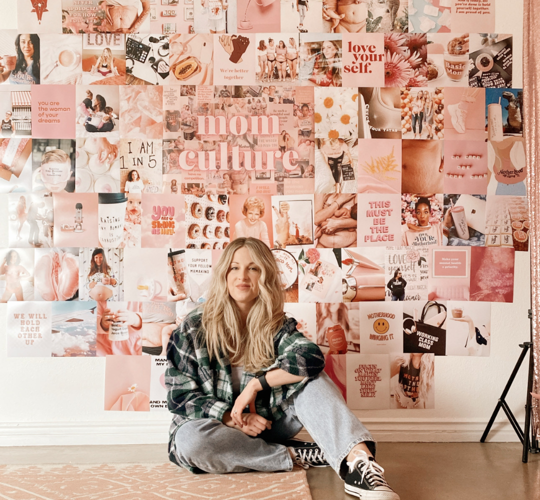 Sarah Komers sitting on the floor in front of a pink collage wall.