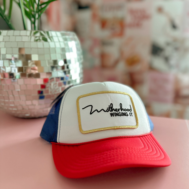 Red, white and blue trucker hat with a “Motherhood Winging It” patch.