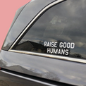 White “Raise Good Humans” decal on a car’s rear side window.