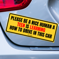 Yellow car magnet reading “Please Be a Nice Human: A Teen Is Learning How to Drive in This Car.”