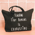 Black tote bag with white “Teaching Tiny Humans Is Exhausting” lettering.
