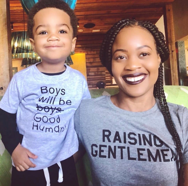 Mother wearing a gray “Raising Gentlemen” T-shirt beside a child.