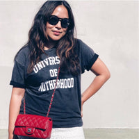 Woman wearing a black “University of Motherhood” T-shirt and a red crossbody bag.